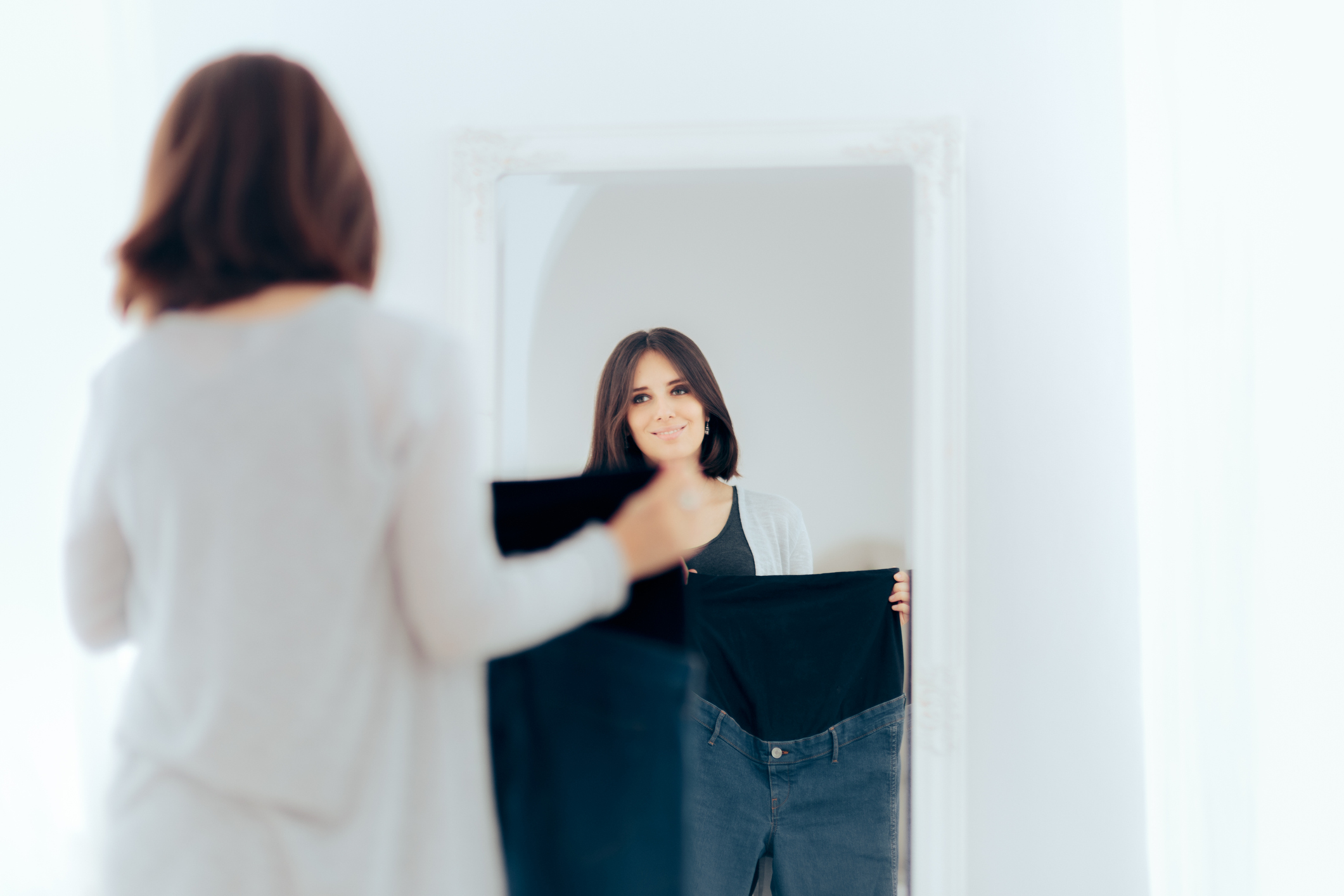 A woman holds up a pair of maternity jeans