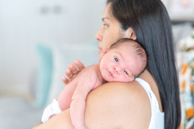 A new mom holds newborn baby over her shoulder at home