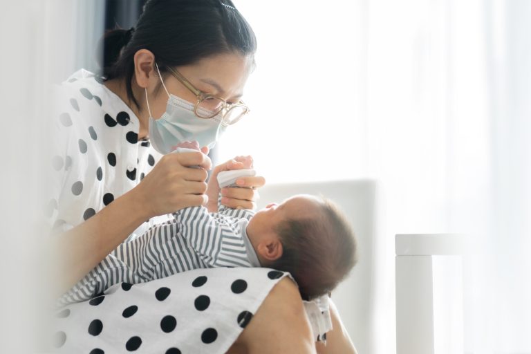 A masked mom plays with her infant