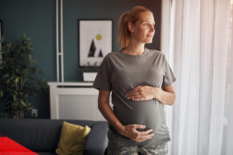 A pregnant woman looks out a window at her home