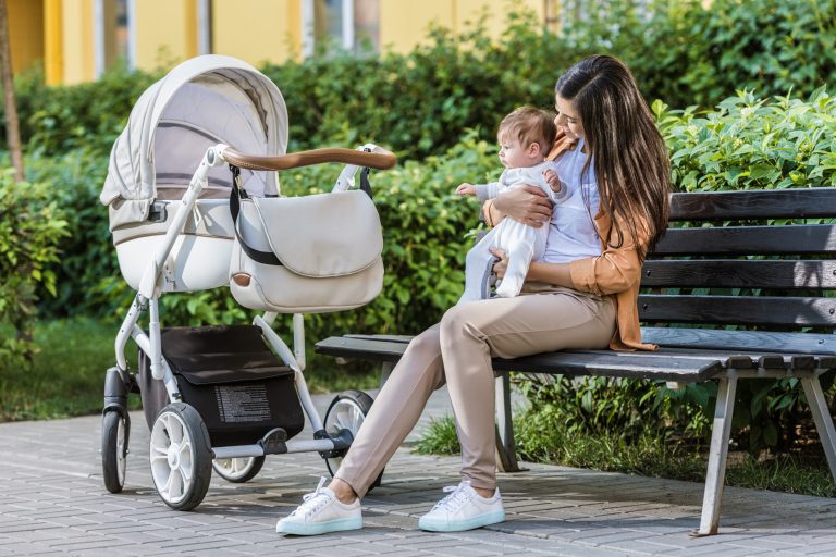 A mom sitting with her baby in a park next to her stroller