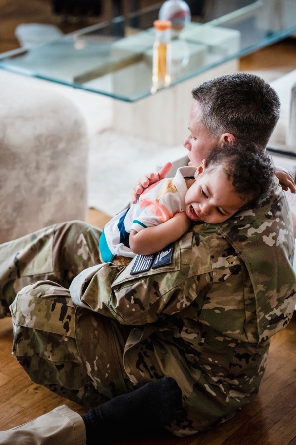 Military mom in uniform hugging her baby at home