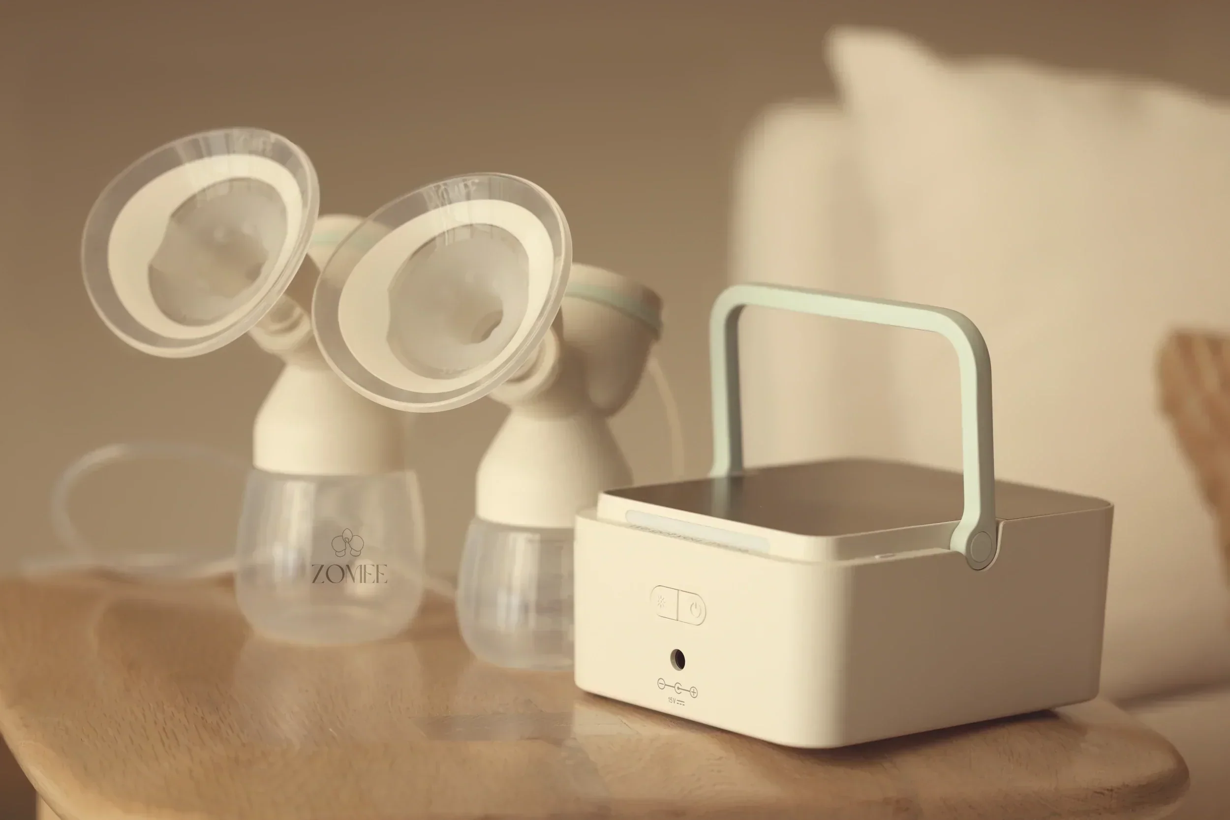 Zomee H1 double electric breast pump with two flanges and carry handle on a wooden bedside table