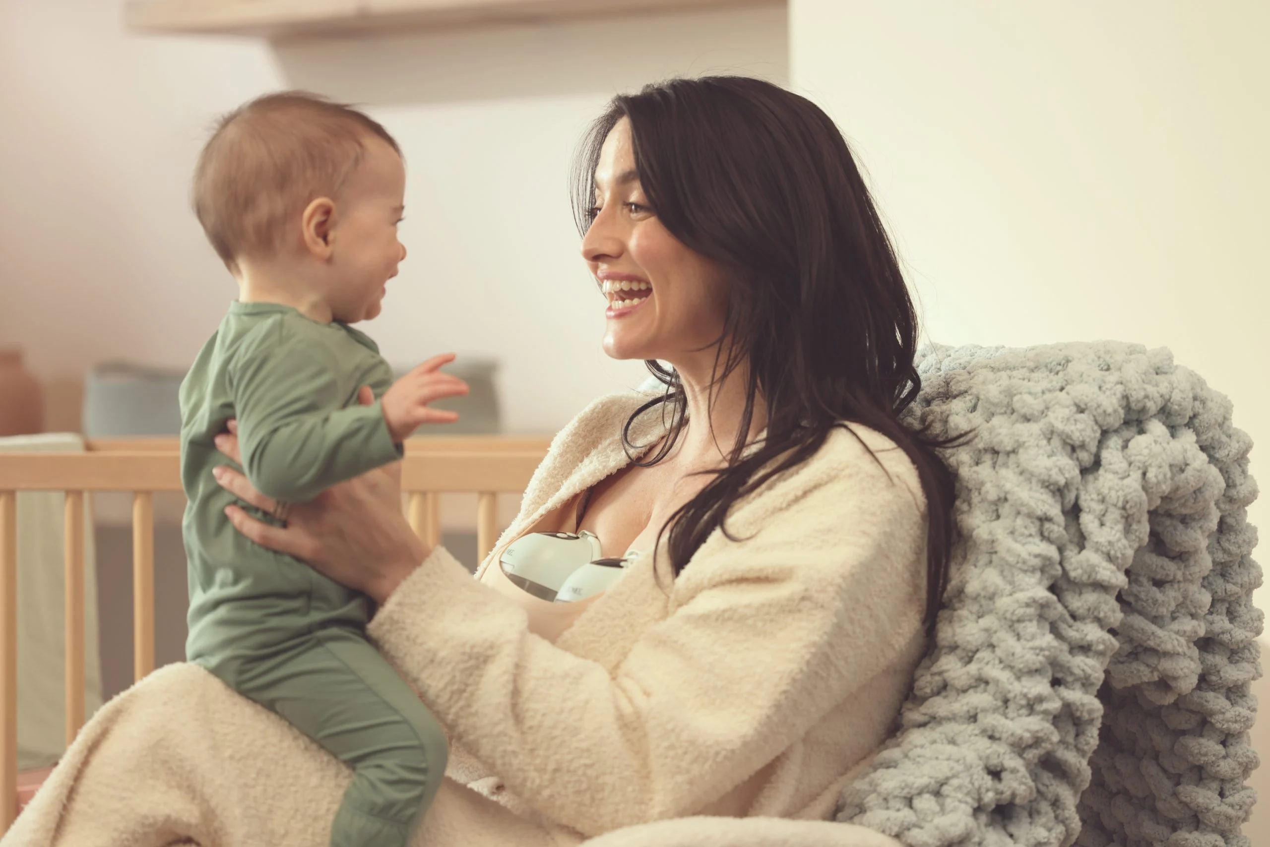 Mother holding baby while using the Zomee Mother’s Nature W1 hands-free wearable breast pump in a comfortable home setting